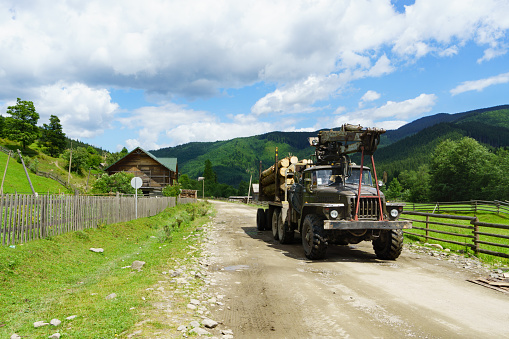 Heavy powerful old military green truck with timber on country mountains road street transporting wood. Firewood as a renewable energy source.