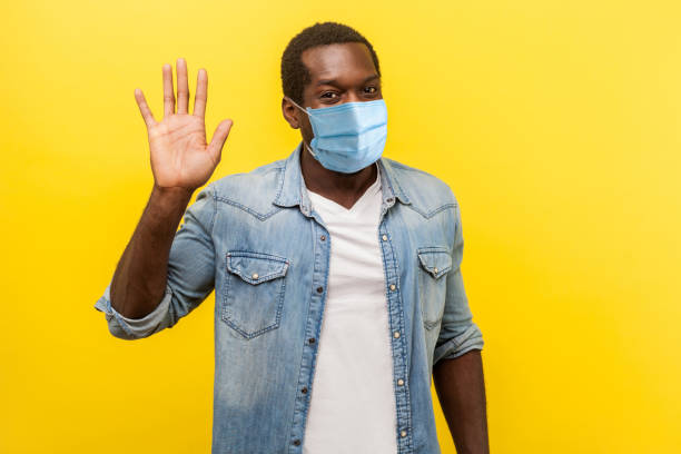 hello! portrait of positive handsome man with medical mask with rolled up sleeves smiling friendly and waving hand saying hi, welcoming gesture. - friends color background imagens e fotografias de stock