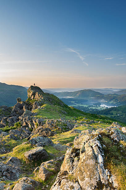Helm Crag at Dawn A walker alone at the summit of Helm Crag, overlooking Grasmere as the sun rises. english lake district stock pictures, royalty-free photos & images