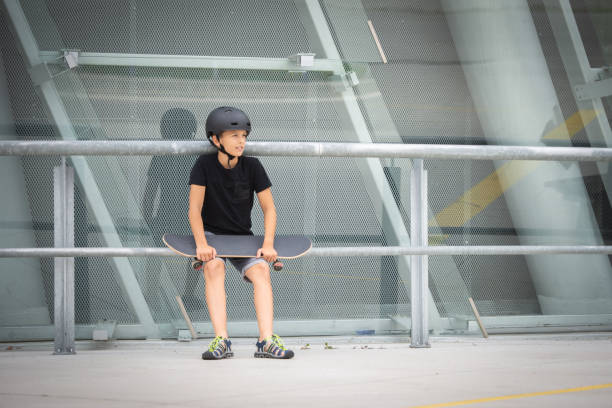 Helmet-fitted brunette teenager skateboard trains on platform in front of concrete building stock photo