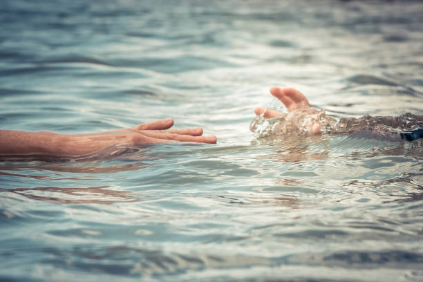 Helping adult hand reaching child hand drowning in water concept water rescue safety stock photo