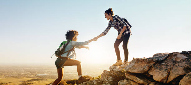 Helping each other to the top of mountain Woman helping her friend to climb the cliff and reach the top of mountain. Friends helping each other during hiking a mountain. a helping hand stock pictures, royalty-free photos & images
