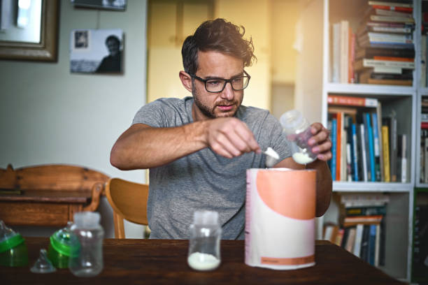 He's learning everyday Cropped shot of a single father preparing a bottle for his baby at home baby formula stock pictures, royalty-free photos & images