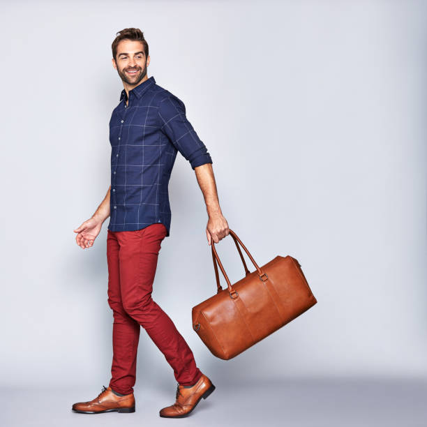 He's off on an adventure Studio shot of a handsome young man carrying a bag against a gray background men's fashion stock pictures, royalty-free photos & images
