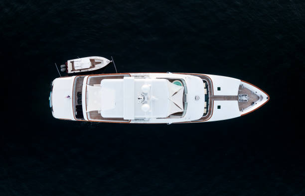 High angle aerial bird's eye view of a long white luxury yacht with wooden deck, a hot tub and a dinghy or tender boat on the side in dark blue waters shortly after sunset in Sydney, Australia. stock photo