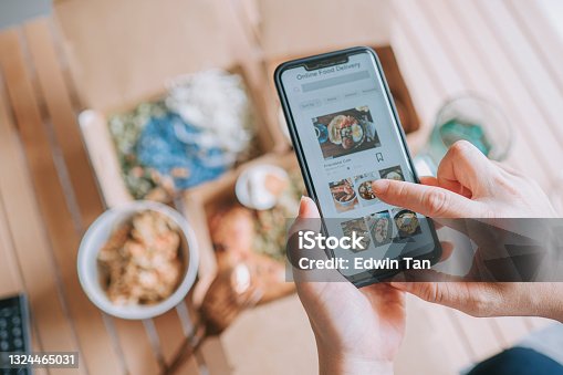 istock high angle view Close up Asian woman using meal delivery service ordering food online with mobile app on smartphone in the living room at a cozy home 1324465031