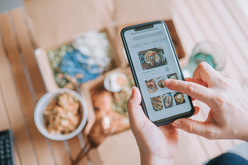 high angle view Close up Asian woman using meal delivery service ordering food online with mobile app on smartphone in the living room at a cozy home