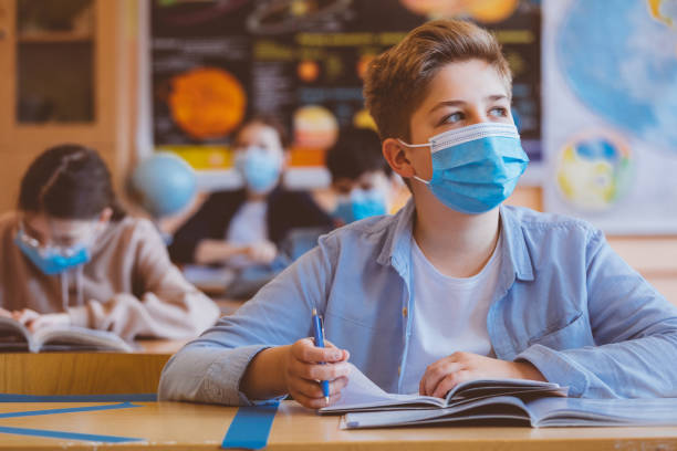 High school boy student at school wearing N95 Face masks High school students at school, wearing N95 Face masks. Teenage boy sitting at the school desk, looking away and thinking. back to school stock pictures, royalty-free photos & images