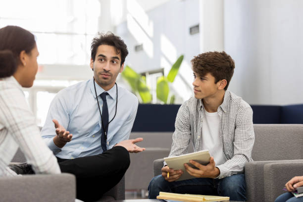 High school counselor talks with students Mid adult male high school counselor gestures while discussing college options with a group of students. school counselor stock pictures, royalty-free photos & images