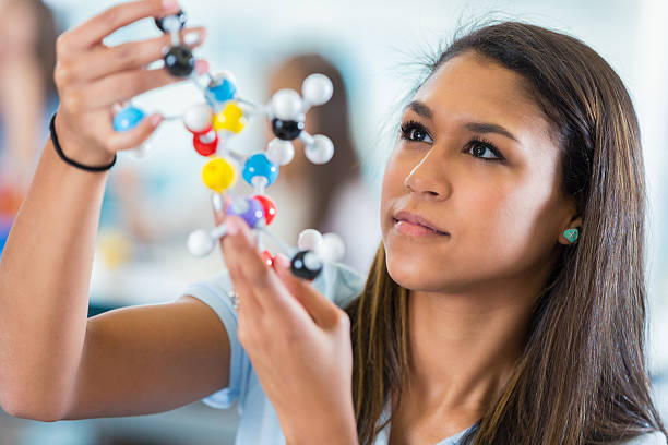 High school girl studying model molecule in science class Hispanic teenage high school girl is concentrating while studying a plastic educational toy model molecule. Student is sitting at a desk in a private high school science lab classroom. chemistry class stock pictures, royalty-free photos & images