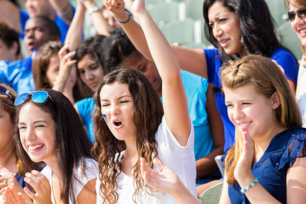 High school sports fans cheering for team in stadium Teenage high school students are cheering for football team while sitting in stands at football stadium. Fans and spectators are watching teams play game and are excited. high school sports stock pictures, royalty-free photos & images