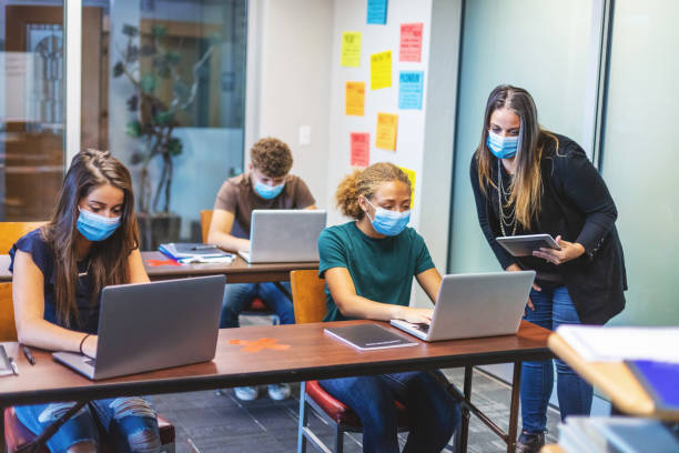 high school students and teacher wearing face masks and social distancing in classroom setting working on laptop technology - teacher back to school imagens e fotografias de stock