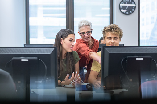A high school professor answers questions from her students as they work on an assignment in the computer lab at their school.