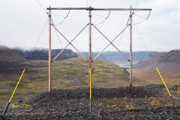 High voltage electrical cables on poles, with a backdrop of a cloudy sky. The lines are attached to the poles with glass insulation. The lines are running through the Icelandic highlands. stock photo