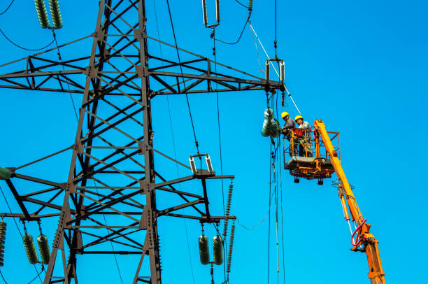 High voltage power line transmission tower workers with crane and blue sky. Hydro linemen on boom lifts working on high voltage power line towers. stock photo