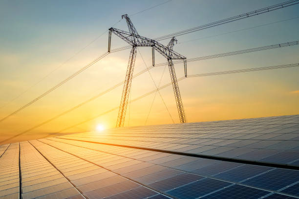 High voltage pylons with electric power lines transfering electricity from solar photovoltaic sells at sunrise. Production of sustainable energy concept. stock photo