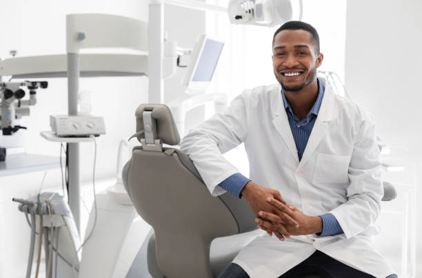 Highly qualified young dentist posing at modern clinic Highly qualified young black dentist posing at clinic over modern cabinet, empty space dentist stock pictures, royalty-free photos & images