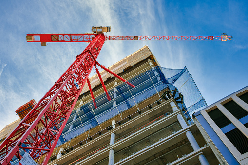 Looking up at the construction site of a high-rise building with red crane in the foreground.