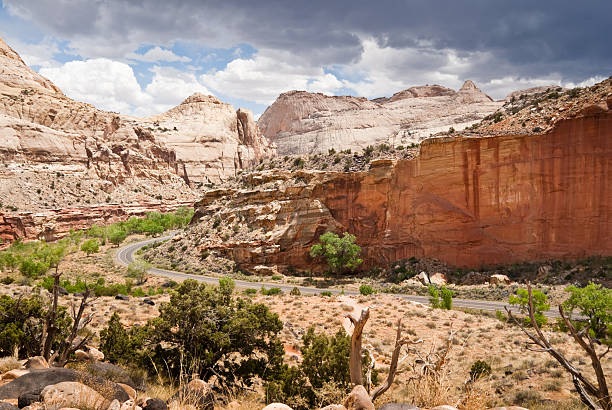 Highway Winding by Capitol Dome Capitol Reef National Park is in the desert of southern Utah. The park is filled with cliffs, towers, domes and arches. The first part of the park’s name derives from the many dome shaped Navajo Sandstone formations each of which resembles the US capitol. The second half of the name refers to the parallel impassable ridges which the early settlers called reefs. The first paved road through this area wasn’t constructed until 1962. Central to the area is the famous Waterpocket Fold, a 100-mile wrinkle in the earth, which is 65 million years old and the largest exposed monocline in North America. The Fremont River has carved canyons through some parts of the Waterpocket Fold but the area remains a dry desert. The park is also a showcase for ancient history and the more recent history of the Mormon pioneers. This scene of a dome shaped sandstone formation was photographed from the Hickman Bridge Trail in Capitol Reef National Park near Fruita, Utah, USA. jeff goulden capitol reef national park stock pictures, royalty-free photos & images