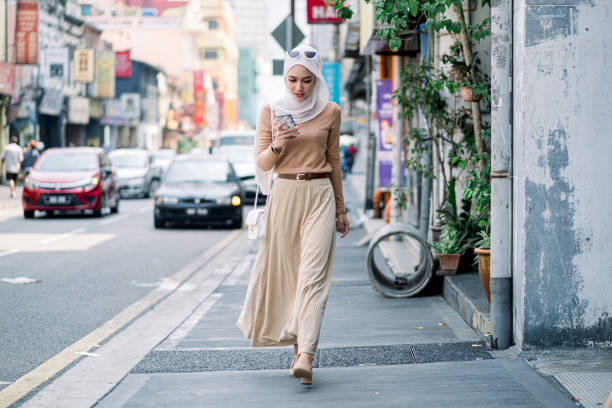 hijab zakenvrouwen gebruiken telefoon tijdens het lopen - business malaysia stockfoto's en -beelden