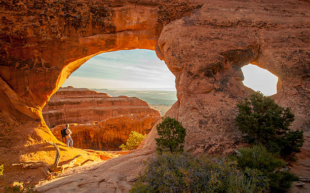 Hiker, Arches National Park, Utah Senior hiker, age 58, stands in contemplation of Double Arch at sunrise, Arches National Park, Utah. arches national park stock pictures, royalty-free photos & images