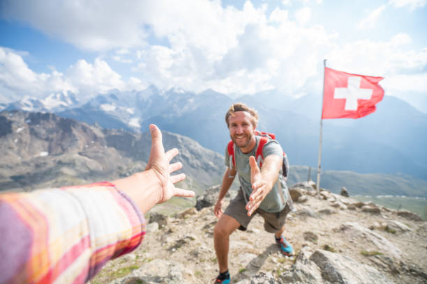 Hiker assisting teammate at mountain top giving a helping hand to reach summit, Switzerland Hiker assisting teammate at mountain top giving a helping hand to reach summit graubunden canton stock pictures, royalty-free photos & images