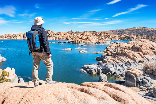 Stock photograph of a hiker with backpack looking at view at Watson Lake, Prescott, Arizona USA on a blue sky day.