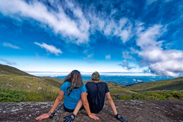 Hiker couple having rest on top of mountain with blue sky and clouds. Adventure travel, couple of hikers relaxing on top of mountain. stock photo