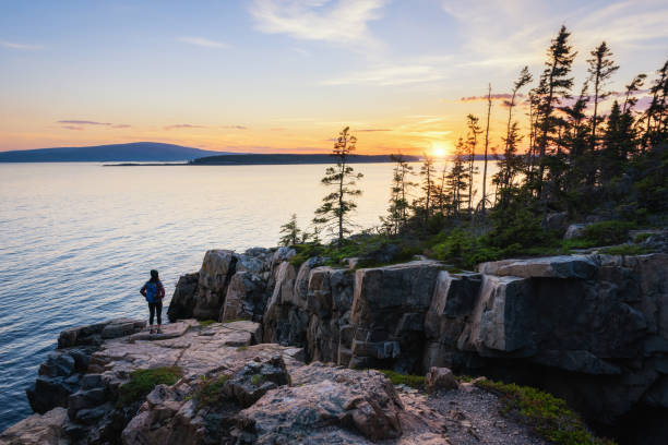 Hiker enjoying the sunset near schoodic point A female hiker watching the setting sun at Ravens Nest on the Schoodic Peninsula in Acadia National Park, Maine. maine stock pictures, royalty-free photos & images