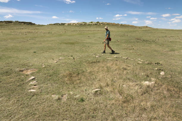 A hiker explores a stone circle or rocks that once held down the edges of a Native American tipi remain in a circle and have sunken into the soil with time on the short grass prairie of Pawnee National Grasslands in northern Colorado.