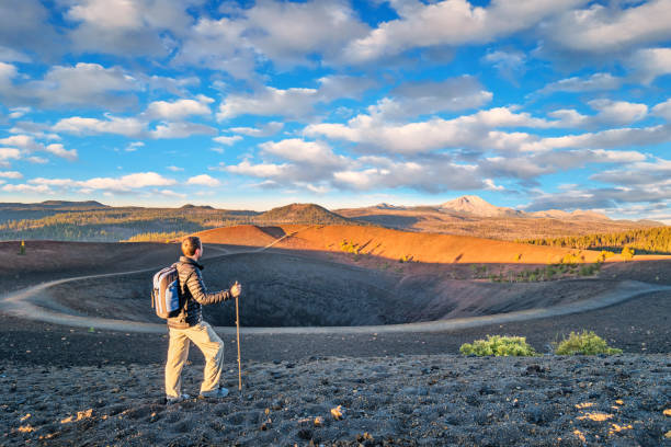 Hiker in Lassen Volcanic National Park California Stock photograph of man hiking on the Cinder Cone Rim in Lassen Volcanic National Park during sunrise, with Lassen Peak in the background. natural landmark stock pictures, royalty-free photos & images