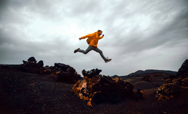 Hiker man jumping over the mountain. Freedom, risk, success and challenge. Focus on man stock photo
