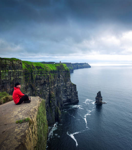 Hiker sitting at the cliffs of Moher Hiker sitting at the cliffs of Moher located at the edge of the Burren region in County Clare, Ireland. cliffs of moher stock pictures, royalty-free photos & images