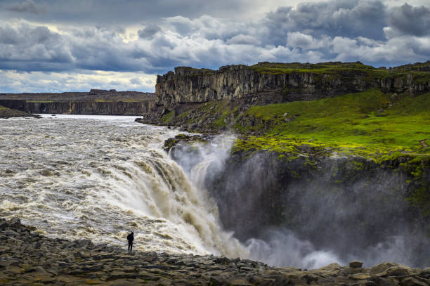 Hiker standing close to the Dettifoss waterfall in Iceland Hiker standing close to the Dettifoss waterfall located on the Jokulsa a Fjollum river in Iceland. Dettifoss is the second most powerful waterfall in Europe after the Rhine Falls. iceland dettifoss stock pictures, royalty-free photos & images