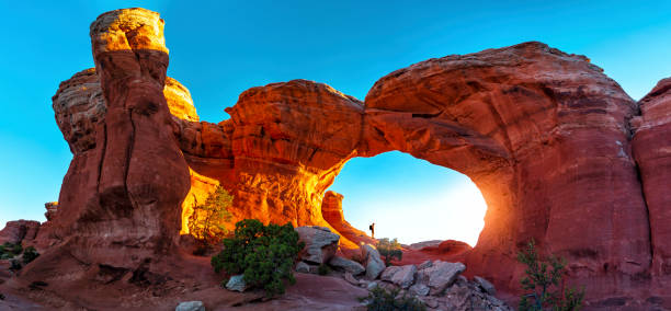 Hiker standing in Turret Arch panoramic A hiker watching the sunrise in Turret Arch, Arches National Park, Utah arches national park stock pictures, royalty-free photos & images