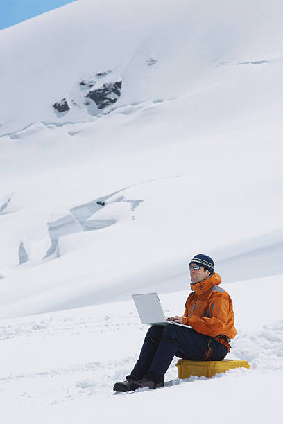 Side view of a male hiker using laptop on snowy mountain landscape