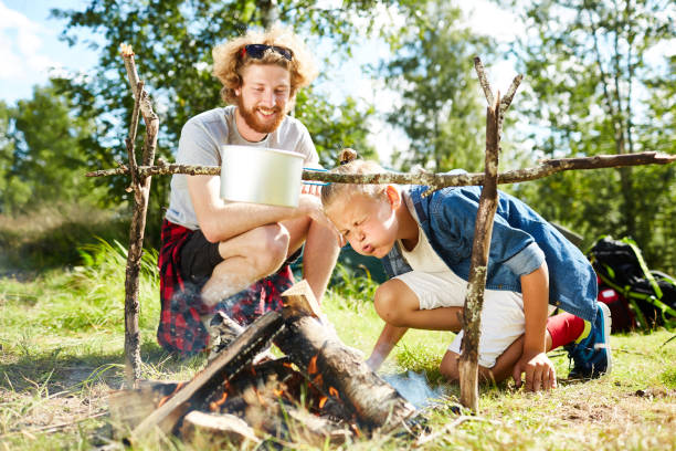 Hikers cooking Funny boy blowing on heap of woods to burn them out while cooking breakfast with his father on trip boy scout camping stock pictures, royalty-free photos & images