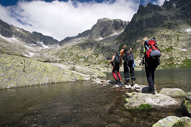 Hiking in high mountains Group of people crossing mountain pond in Tatra Mountains, Slovakia slovakia stock pictures, royalty-free photos & images