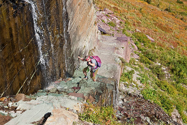 Hiking the Waterfall Ledge on the Grinnell Glacier Trail The Waterfall Ledge is a short stretch of the Grinnell Glacier Trail. The waterfall cascades down a rock ledge and across the trail. This woman is carefull hiking up the steps that were carved by the running water. The Waterfall Ledge is in Glacier National Park, Montana, USA. jeff goulden montana stock pictures, royalty-free photos & images