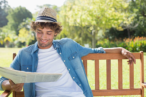 moda giovane uomo seduto sulla panchina nel parco lettura giornale - young man read newspaper foto e immagini stock