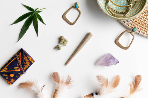 Hippy Festival Essentials on White and Wicker with Joint, Buds, Feathers, Turquoise, Marijuana Leaf, Amethyst Crystal and a Celestial Weed Pouch - Top Down stock photo