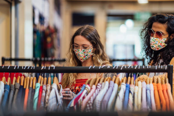 Hipster Couple Thrift Shopping in Reusable Protective Face Masks A shot of a young caucasian hipster woman and her mid adult Pakistani boyfriend looking at second hand, recycled clothing at a small local business in a market. They are wearing casual bohemian clothing, accessories, eyewear and reusable protective face masks. thrift store stock pictures, royalty-free photos & images