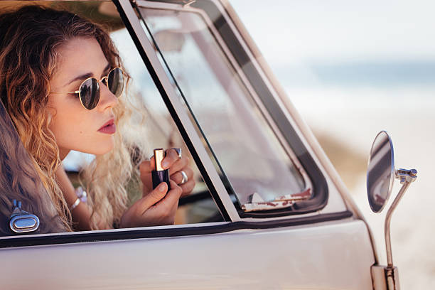 Hipster Girl Putting on Lipstick in Sideview Mirror of van stock photo