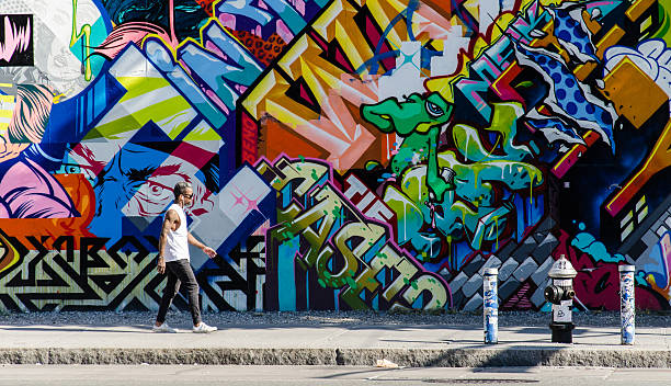Hipster male walking next to wall of graffiti in Brooklyn New York City, NY, USA - October 1, 2013: Hipster male walking next to a wall of graffiti in Brooklyn, New York, US. graffiti stock pictures, royalty-free photos & images