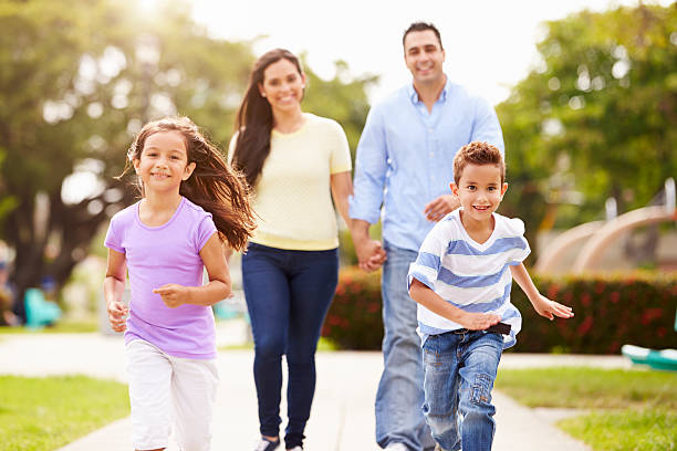 Hispanic Family Walking In Park Together Hispanic Family Walking In Park Together Children Running Ahead Smiling four people stock pictures, royalty-free photos & images