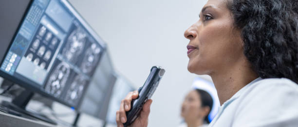Hispanic female medical professional viewing MRI scan and recording report on dictaphone. stock photo