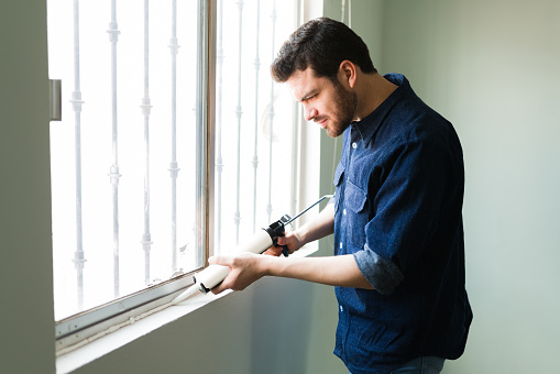 Attractive young man and handyman insulating his home windows during the winter season