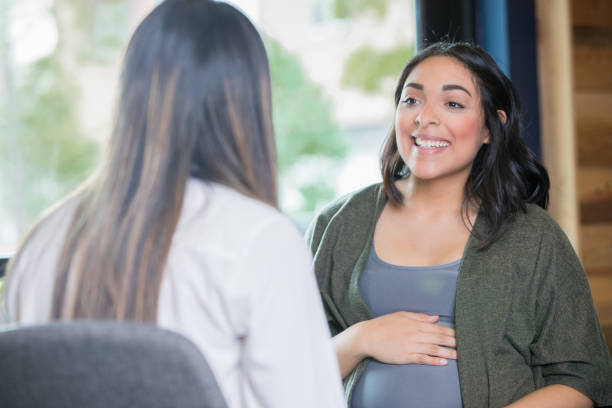 Hispanic woman discussing her pregnancy with midwife Young adult Hispanic expectant mother is discussing her pregnancy with a midwife during a support group meeting or childbirth class. midwife stock pictures, royalty-free photos & images