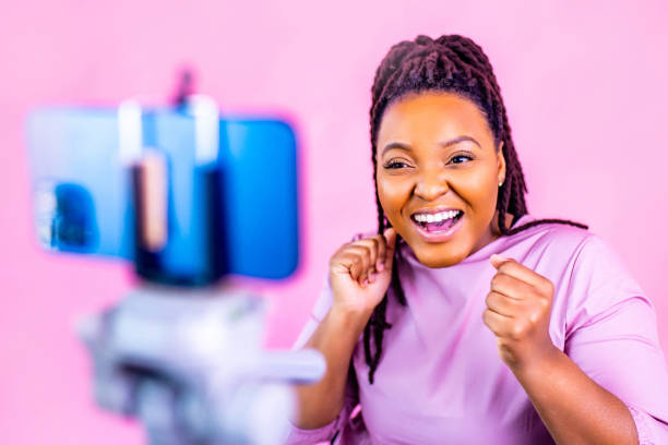 hispanic woman with cool dreadlocks pigtails wear pink dress in studio chatting with her subscribers by phone camera stock photo