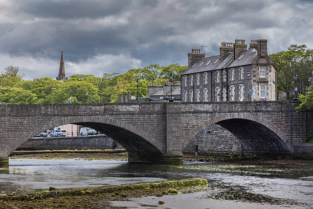 Historic bridge in Wick, Scotland. Wick, Scotland - June 4, 2012: Historic bow gray stone bridge over shallow Wick River downtown under rainy cloudy skies. Green foliage of trees and gray stone hotel in background. Look through the bows. caithness stock pictures, royalty-free photos & images